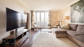 A modern living room with a flat-screen TV, a sectional sofa, a white armchair, and a large window with curtains. - Magnificent apartment between Paris and Disneyland. Rer A 10 min by bus -PARKING  (Neuilly-sur-Marne)
