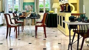 Un'ampia sala da pranzo con soffitto alto, un tavolo centrale con sedie e un armadietto giallo con vetrate.