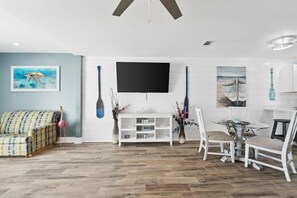 Een woonkamer met een bank, een televisie, een eettafel met stoelen en kunstwerken aan de muur.