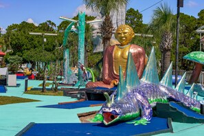 Een groot gouden Boeddhabeeld, omringd door kleurrijke sculpturen en een tropische tuin.