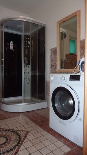 A corner room with a glass-enclosed shower, a washing machine, and a tiled floor.