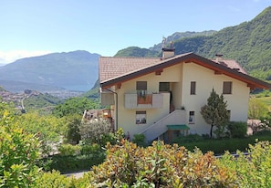 A two-story house with a balcony, surrounded by greenery and mountains. - Holiday apartment with terrace and parking (Tenno)