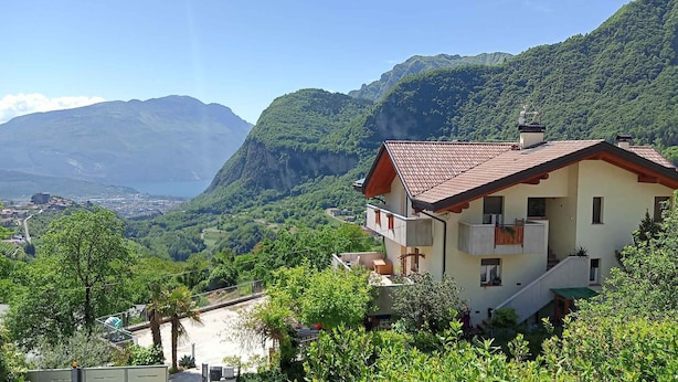 Una casa de dos pisos con techo de tejas rojas, un balcón y vistas a un valle y montañas.