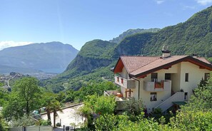 A two-story house with a red-tiled roof, a balcony, and a view of a valley and mountains. - Holiday apartment with terrace and parking (Tenno)