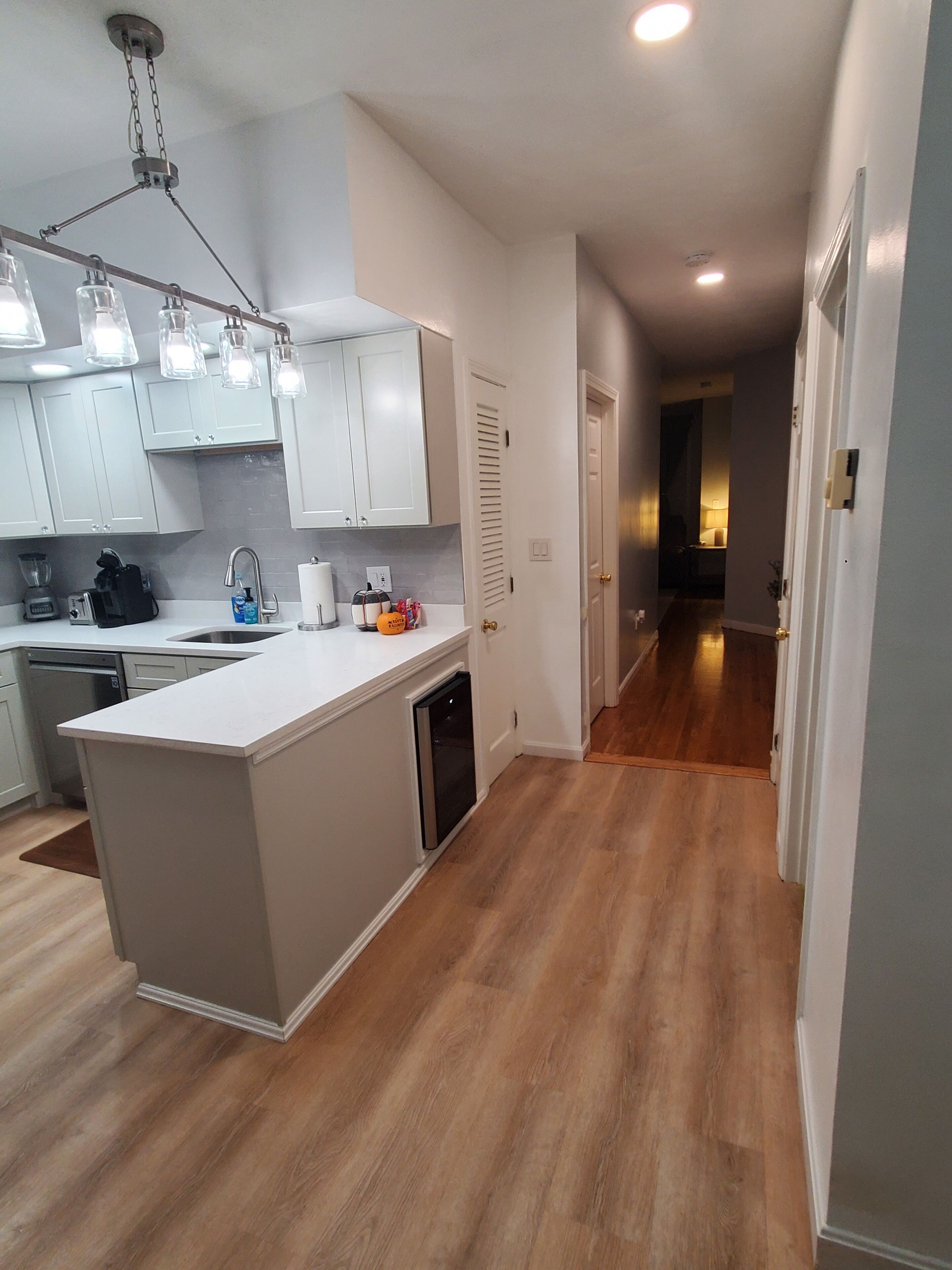 A modern kitchen with white cabinets, a central island, and a wooden floor.