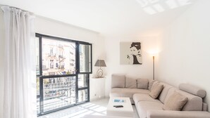 A modern living room with a large window, a sofa, a coffee table, and a lamp. - Rue d'Antibes Premium 2 BDR 2 baths Exclusive Olam Properties Cannes (Cannes)