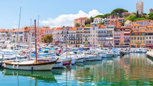 A marina with numerous boats docked, colorful buildings in the background, and a prominent tower on a hill. - Rue d'Antibes Premium 2 BDR 2 baths Exclusive Olam Properties Cannes (Cannes)