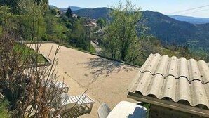 A patio area with a table and chairs, surrounded by trees and a view of distant hills. - The Vault of the Stars overlooks the Monts d’Ardèche (Genestelle)