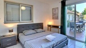 A bedroom with a bed, bedside table, lamp, and a view of an outdoor dining area. - The Vault of the Stars overlooks the Monts d’Ardèche (Genestelle)