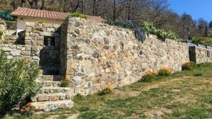 A stone wall with a small building on top, surrounded by trees and grass. - The Vault of the Stars overlooks the Monts d’Ardèche (Genestelle)