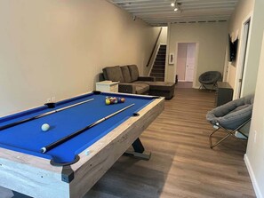 A pool table in a room with a staircase, a sofa, and a chair. - House at Maple Ridge, perfect for long stays. (Monaca)