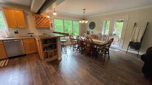 Un'ampia cucina con mobili in legno, una zona pranzo con un tavolo e sedie di grandi dimensioni e vista sull'esterno attraverso ampie finestre.