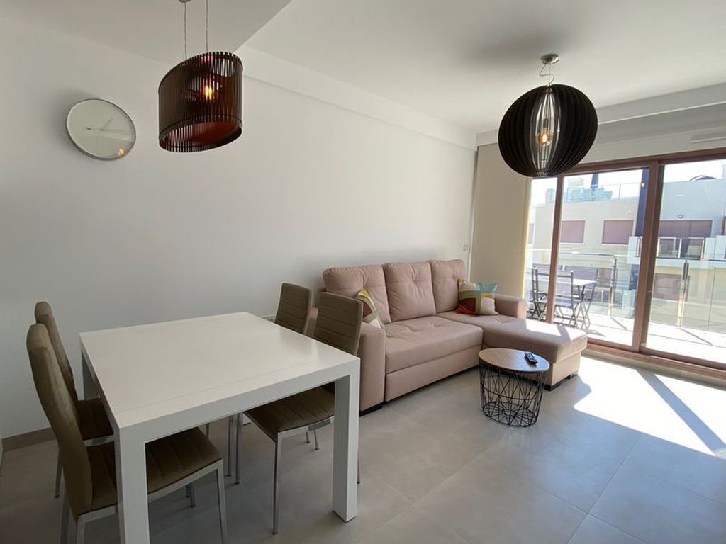 Un salon moderne avec une table à manger blanche, un canapé beige et deux luminaires suspendus.