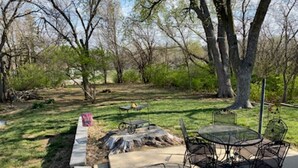 An outdoor patio with a table and chairs, surrounded by trees and a grassy area. - Four Bedroom Bellevue Beauty (Bellevue)