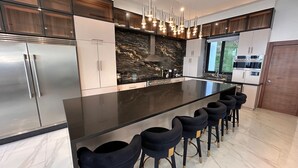 Een moderne keuken met een groot eiland, roestvrijstalen apparatuur en een aanrecht van natuursteen.
