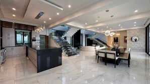 Een moderne keuken met een centraal eiland, een eetgedeelte met een marmeren vloer en een trap naar een hoger gelegen verdieping.