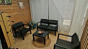 A room with a wooden floor, two black chairs, a small table with a decorative bowl, and a string of lights on the ceiling.
