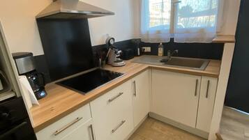 Une petite cuisine équipée d’une cuisinière, d’un évier et d’une fenêtre avec des rideaux.