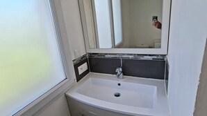 A bathroom with a white sink, a mirror, and a window.