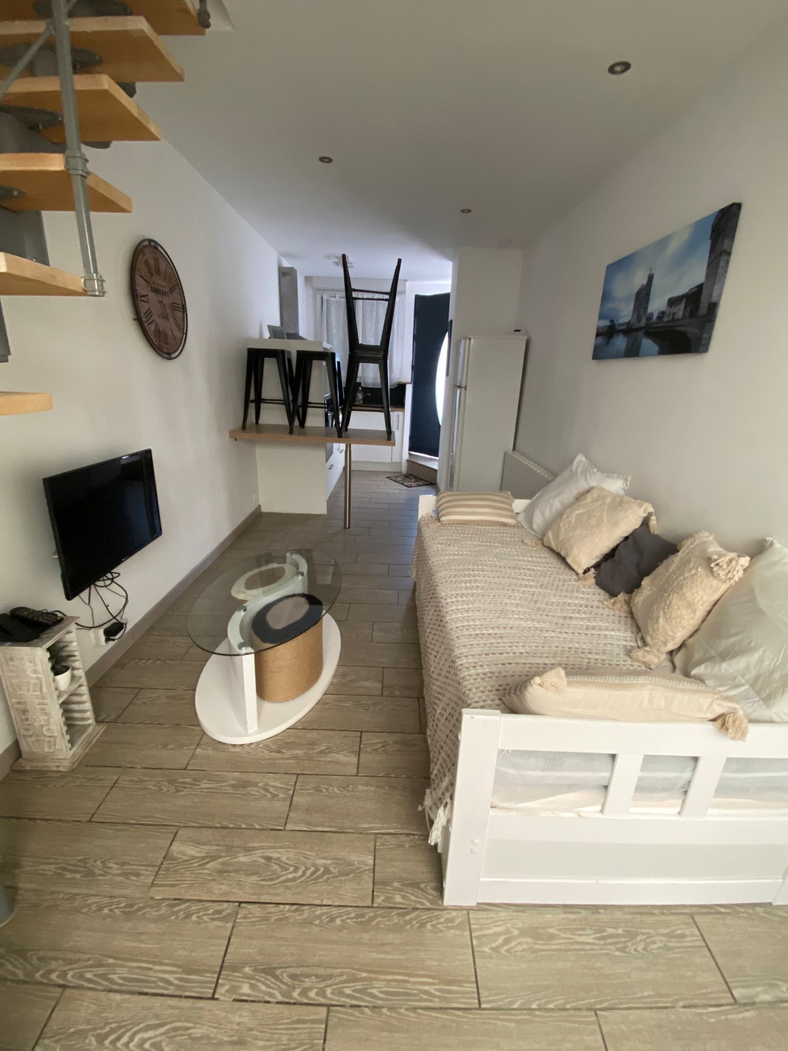 Un salon avec un canapé, un téléviseur et une table basse. Un escalier mène à une autre pièce.