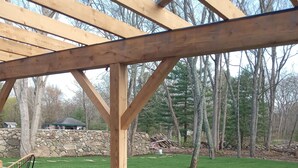 Un patio al aire libre con una pérgola de madera, un sofá con cojines grises y una mesa de mimbre.