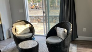 Un salón moderno con dos sillones de mimbre, una mesita redonda y vistas a un espacio exterior con pared de piedra y árboles.