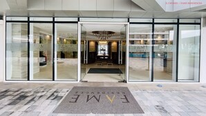 A hotel entrance with a glass facade, a reception desk, and a chandelier.