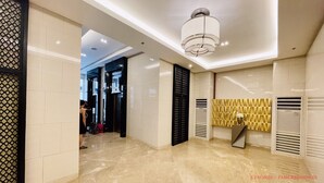A modern hotel lobby with a high ceiling, a central chandelier, and a patterned wall.