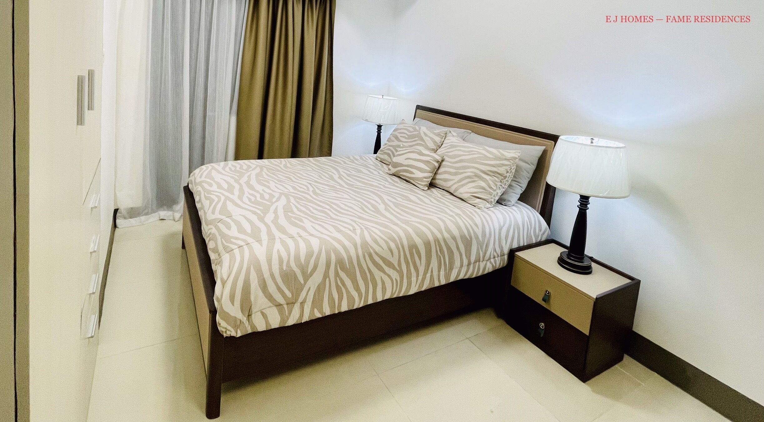Een netjes opgemaakt bed met een bedspreide en kussens met een zebraprint, een nachtkastje met een lamp, en een deur met een gordijn.