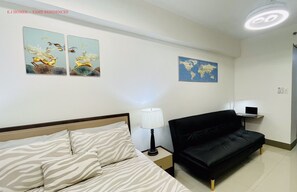 Et hotelværelse med en seng, en sort sofa, et natbord med en lampe, et verdenskort på væggen og to billeder af fugle.