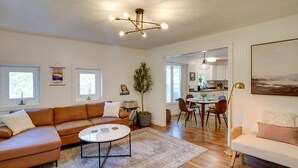 A spacious living room with a large brown sectional sofa, a white round coffee table, and a dining area with a table and chairs. - Mid-Century Modern Fayetteville Home Close to Town (Fayetteville)