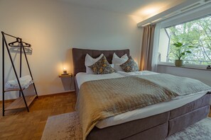 A bedroom with a bed, a bedside table, a hanging light, a window with a view, and a wooden floor. - Studio apartment with parking (Esslingen am Neckar)