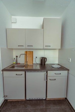A compact kitchen with a sink, a kettle, and cabinets. - Studio apartment with parking (Esslingen am Neckar)