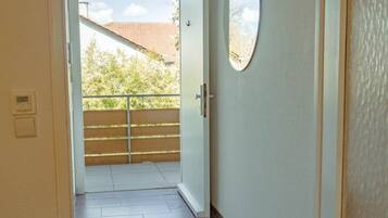 Ein Flur mit Holzboden, einem kleinen Teppich und einer Tür, die auf einen Balkon mit Blick auf Bäume und ein Gebäude führt.