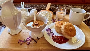 A breakfast setting with a pitcher, a bowl of honey, biscuits, jam, and a candle.