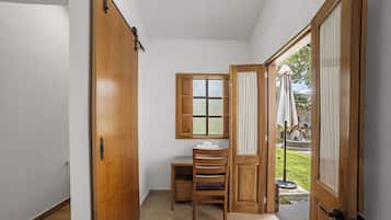 A narrow hallway with a wooden door, a window with frosted glass, a wooden chair, and a small table with a towel.