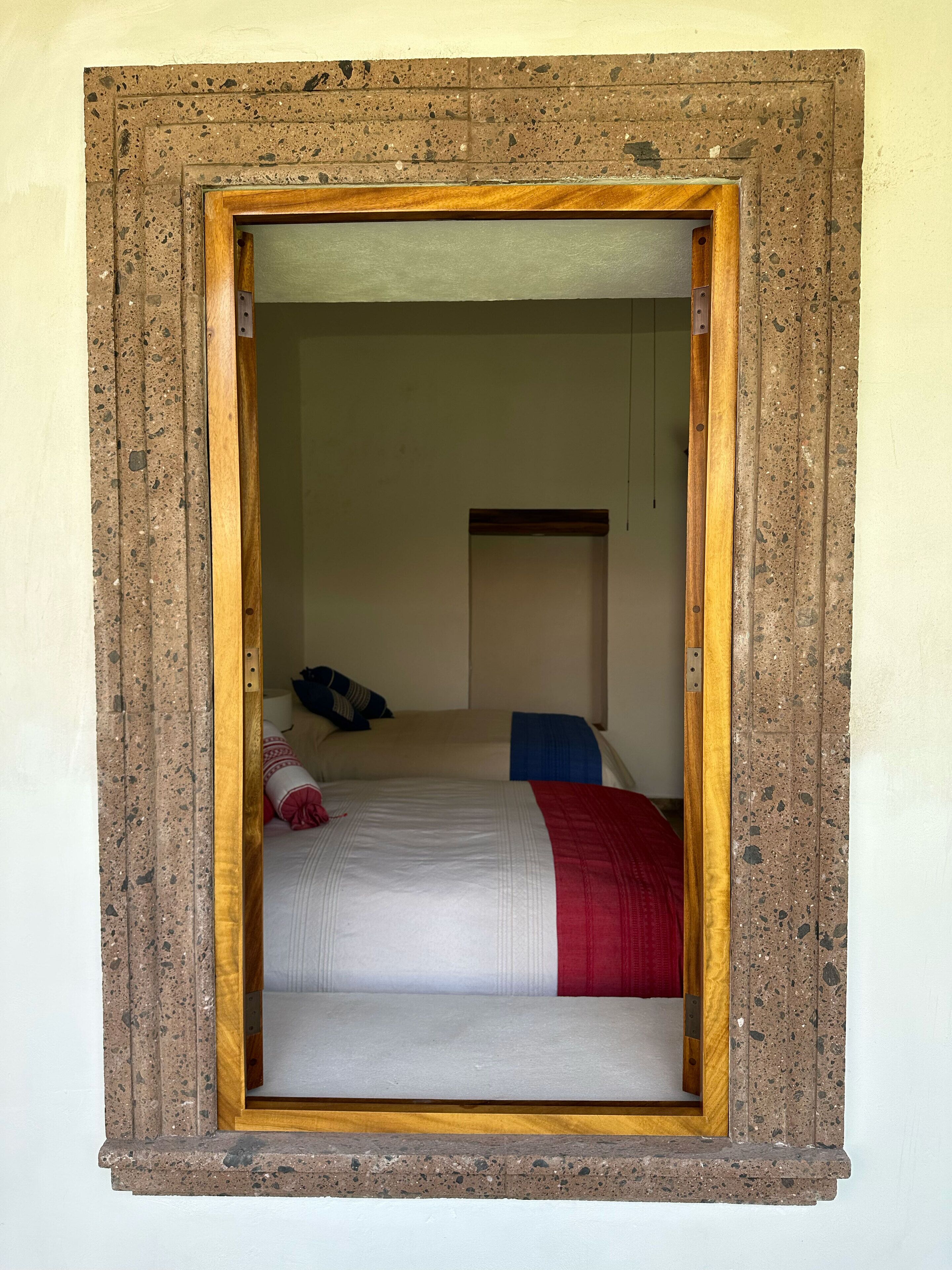 A room with a bed, a wooden headboard, and a window with a wooden frame.