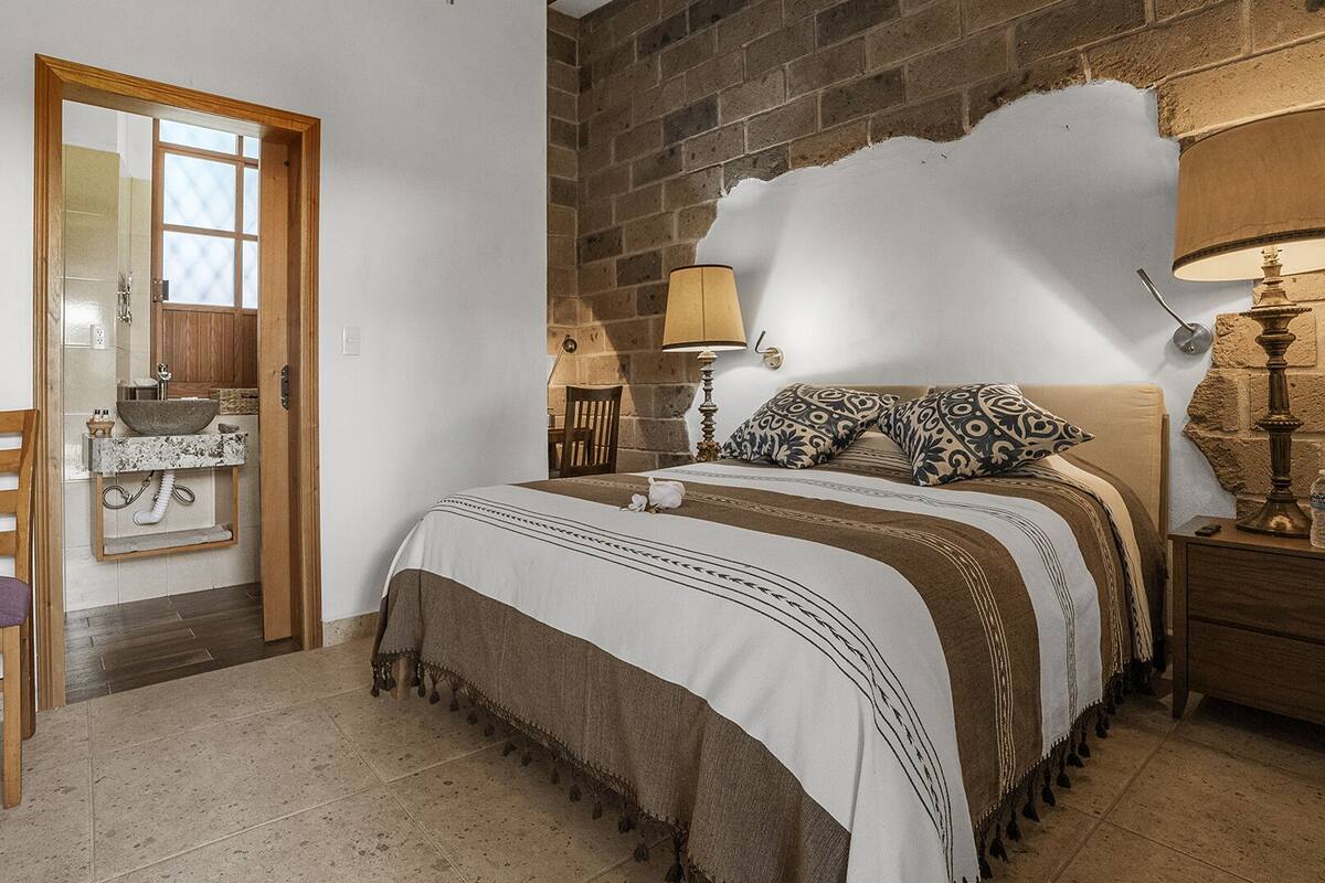 Une chambre à coucher avec un lit, des lampes de chevet, une chaise, une porte en bois et un mur en pierre.