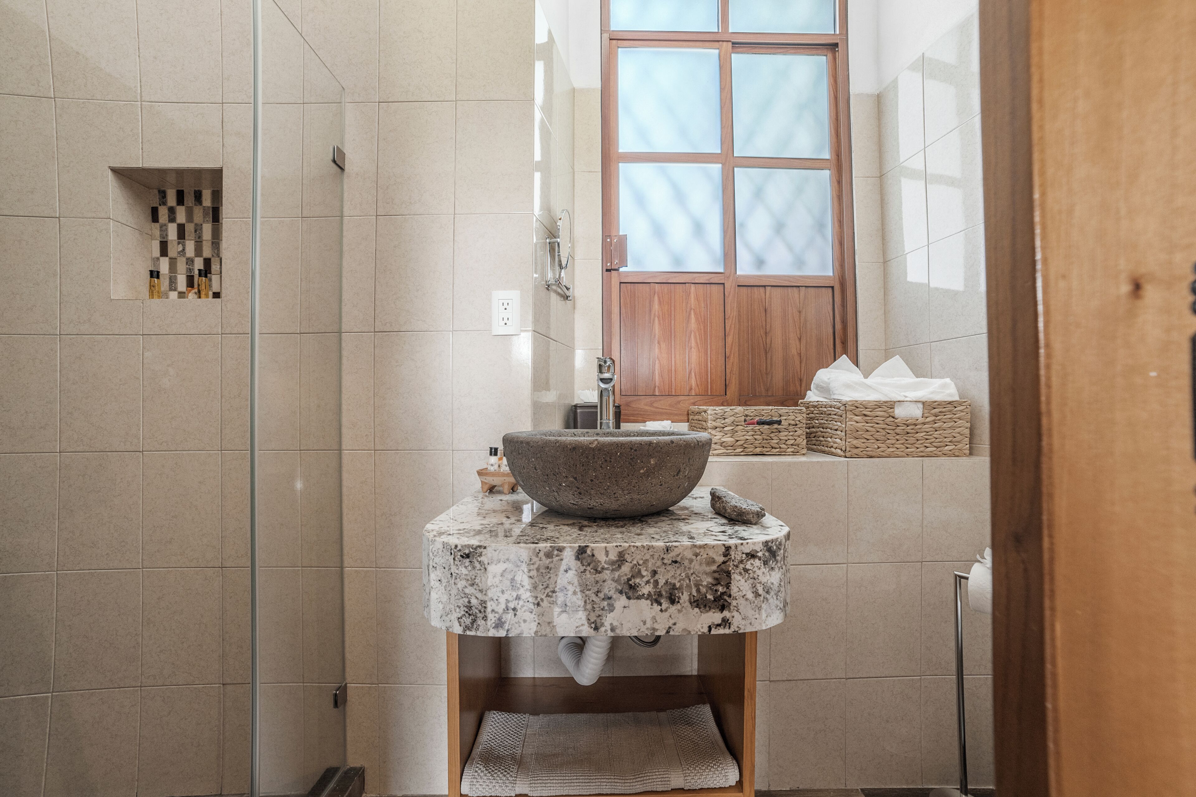 A bathroom with a stone basin, tiled walls, a wooden door, and a window.