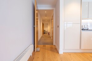 A corridor with wooden flooring, white walls, and a kitchen area with white cabinets and a countertop. - Square Green (No 16) | With Balcony (St Andrews)
