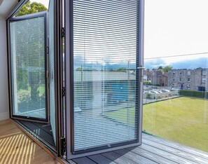 A balcony with a view of a residential area, featuring a sliding glass door and a wooden deck.