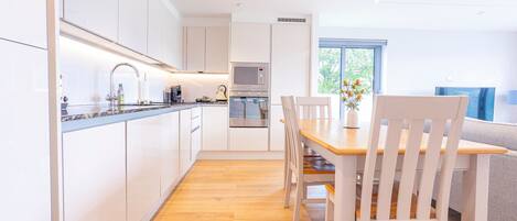 Una cocina moderna con armarios blancos, una mesa de comedor de madera y vistas al exterior.