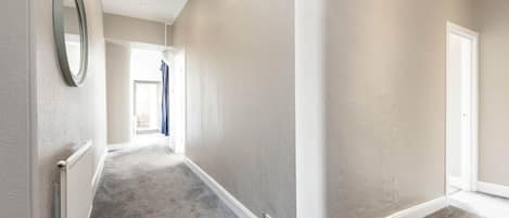 A hallway with a radiator, a mirror, and a door at the end.