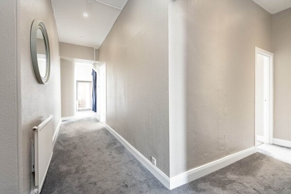 A hallway with a radiator, a mirror, and a door at the end. - Market Street Apartment (No 86D) (St Andrews)