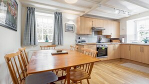 Una cocina con armarios de madera, una mesa de comedor con sillas, una ventana con cortinas y un candelabro en el techo.