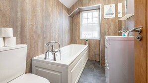 Un baño moderno con bañera, inodoro y lavamanos, con paneles de madera en las paredes y una ventana.