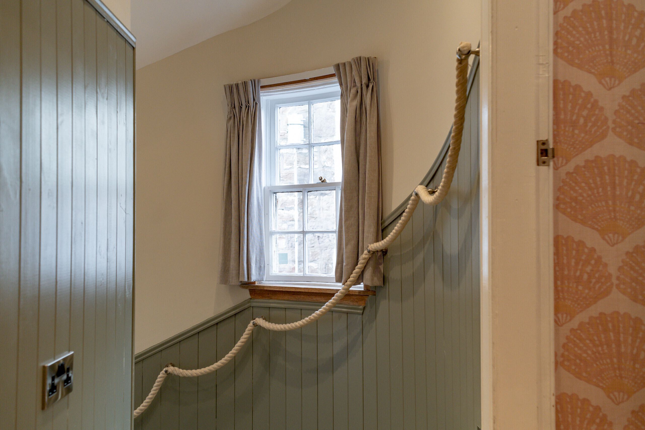 A staircase with a rope barrier, a window with curtains, and a patterned wall.