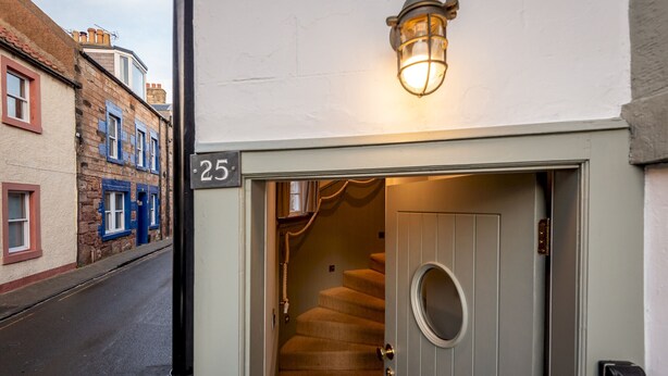 Une entrée d’immeuble avec une plaque portant le numéro « 25 », un escalier et un luminaire au-dessus de la porte.