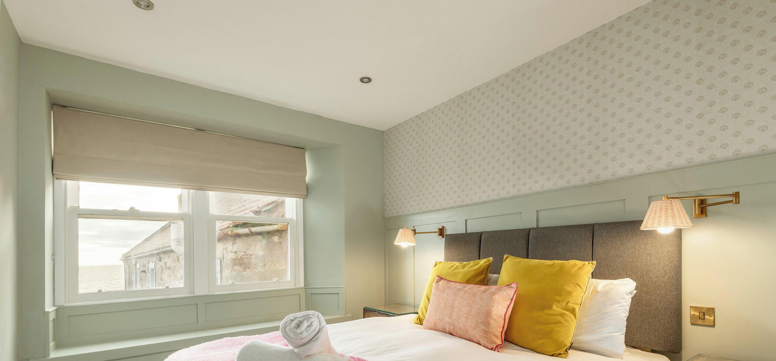 A hotel room with a bed, a window with a view, and two wall-mounted lamps.