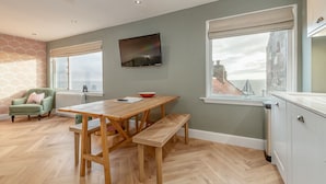 Une cuisine moderne avec un plancher en bois, une table à manger avec des bancs, un fauteuil vert et une vue sur un pont par la fenêtre.